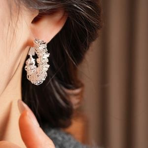 Detail of silver woven texture hoop earring worn by a model in a warm setting