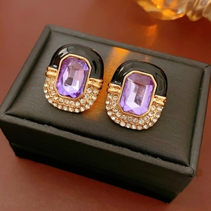 Detail of vintage gold earrings with purple gemstone, rhinestones and black enamel