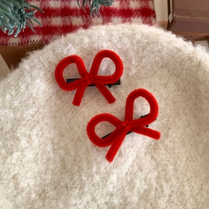 Pair of red chenille bow hair clips on festive background for minimalist winter styling