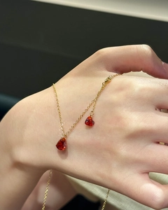 Detail of double heart pendants with red zircon on a golden chain worn on hand