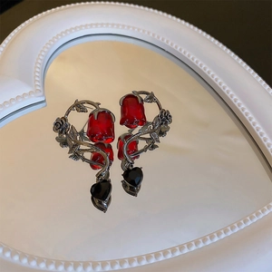 Close-up of red rose stud earrings with black heart charms and silver thorn details