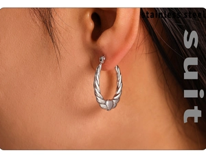 Close-up of twisted stainless steel hoop earring with heart charm on female model