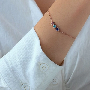 Detailed view of a rose gold chain bracelet with three colorful stones on a wrist