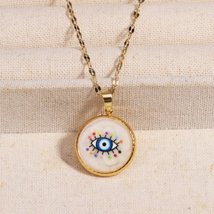 Golden stainless steel Evil Eye pendant necklace with blue eye and colorful dots on beige fabric