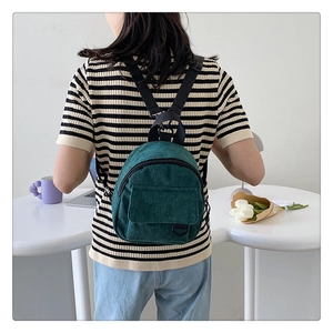 Dark green corduroy mini backpack shown on model in a bright minimalist setting
