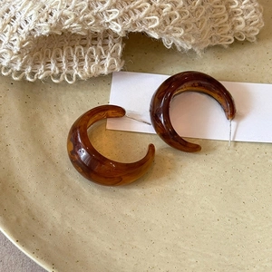 Macro shot of amber resin geometric C-shaped earrings on a ceramic dish and knit background
