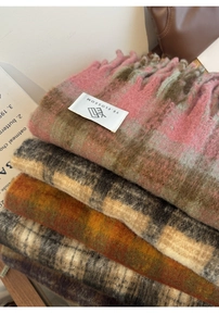 Close-up of stacked thick plaid scarves with fringes in various colors and soft texture