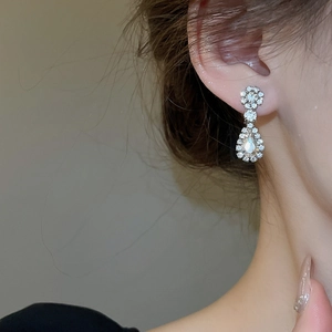 Close-up of sparkling flower and teardrop rhinestone earrings on model for bridal look