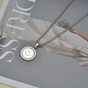 Detail of silver smiley face pendant on a stainless steel box chain over a magazine
