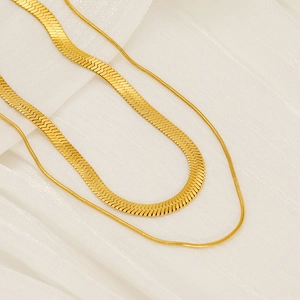Detail of layered gold snake bone chain and thin round necklace on white fabric