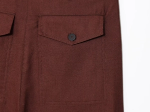 Detail of dark brown linen-textured fabric showing a flap pocket with a black button