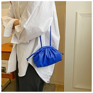 Detail of bright blue cloud pouch bag with thin strap over a white oversized shirt