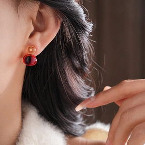 Detail shot of a model wearing amber and burgundy resin gourd earrings with double beads