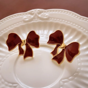 Macro shot of dark red enamel bow earrings with gold plating on a white ceramic plate