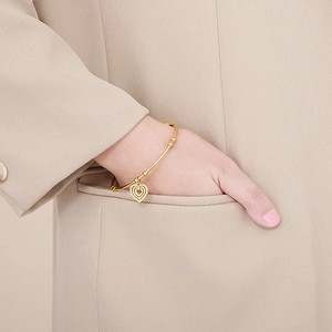 Detail of a thin gold bangle featuring a triple-layered hollow heart pendant on a model
