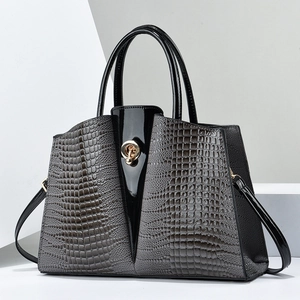 Detail of dark grey crocodile embossed leather handbag with black patent leather and gold lock