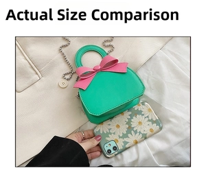 Mini green leather handbag with pink bow shown next to a smartphone for size comparison