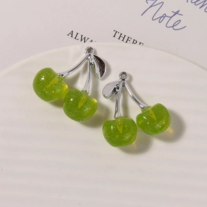 Detail of green cherry charms with gold glitter and silver leaf on a white ceramic plate