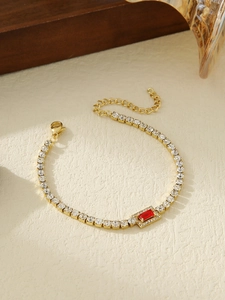 Detailed close-up of gold titanium bracelet with red gemstone pendant and zircon accents