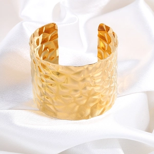 Close-up of golden wide cuff bracelet with a modern hammered texture on a white satin base