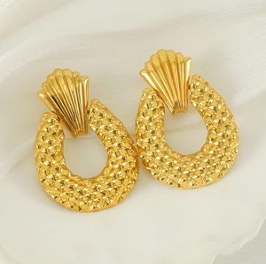 Détail de boucles d'oreilles dorées avec motif losange évidé et texture mate
