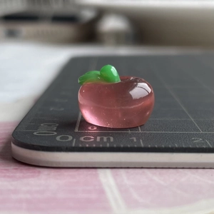 Macro shot showing 1cm mini pink resin apple charm with green leaf for DIY crafts