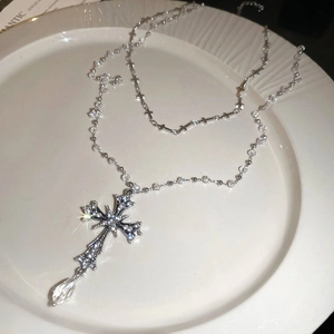 Close-up of a double-layered silver cross pendant with sparkling crystals and a water drop bead