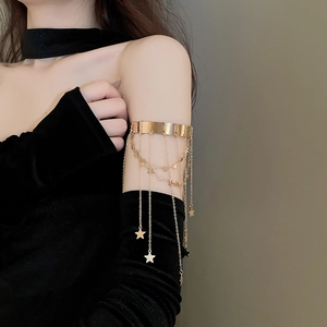 Detailed view of golden arm cuff with hanging metal chains and star charms on model