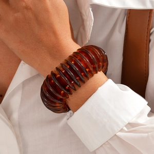 Detail of wide amber acrylic bangle with wavy pleated texture on a white shirt sleeve