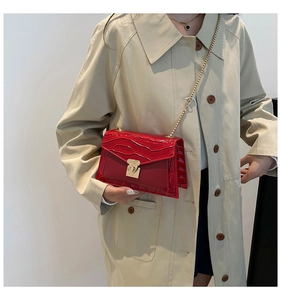 Red crocodile pattern square bag with gold chain strap shown on a beige trench coat