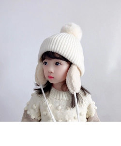 Close-up of children's cream knit earflap hat with soft fleece lining and fluffy pom-pom