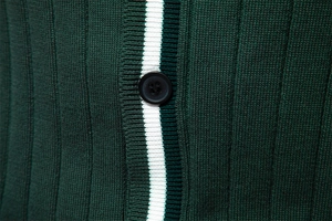 Dettaglio del cardigan in maglia verde bosco con riga a contrasto bianca e bottone nero