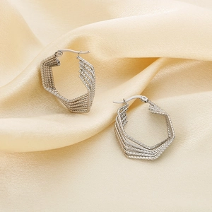 Detailed close-up of silver geometric multi-layer hexagonal earrings on silk fabric