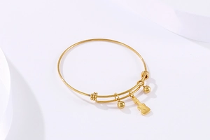 Detailed close-up of a gold stainless steel bangle with guitar and bead charms on white silk