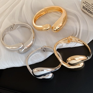 Polished gold and silver teardrop bangles shown on white silk with elegant lighting