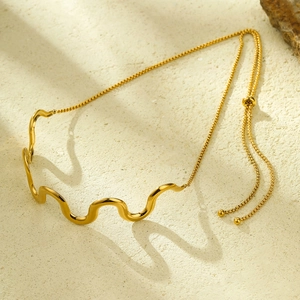 Detail of 18K gold wave pendant necklace with adjustable chain on textured sand background