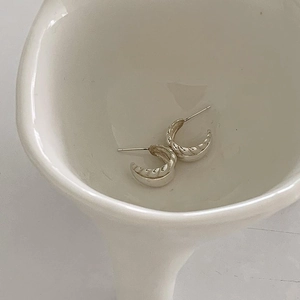 Macro shot of silver croissant hoop earrings displayed on a white ceramic plate