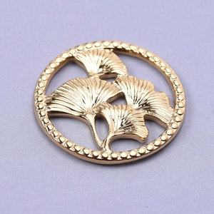 Macro shot of gold stainless steel circular pendant with hollow ginkgo leaf pattern