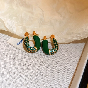 Detailed shot of green enamel U-shaped earrings with zircons on beige fabric