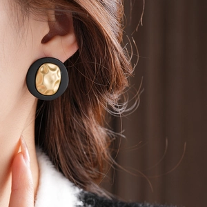 Close-up of retro black matte earrings with textured gold inner metal on model