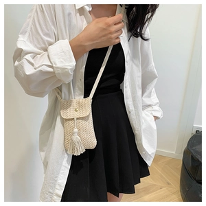 Detailed view of beige woven crossbody bag with tassel detail worn by model