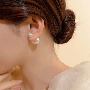 Close-up of elegant double-sided white pearl earrings worn by a model in soft light
