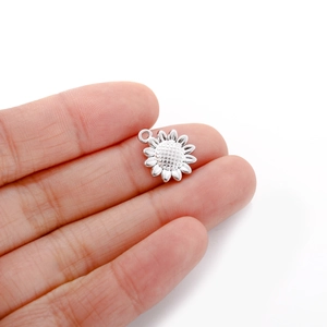 Macro shot showing the actual size of a polished stainless steel sunflower pendant on a finger