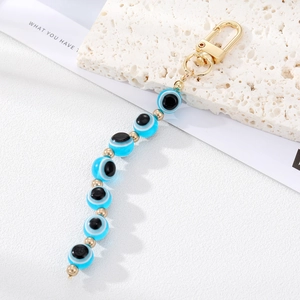 Blue evil eye beaded keychain with gold accents on white marble stone background