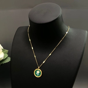 Détail d'un collier doré avec pendentif floral en émail vert sur un buste de mannequin