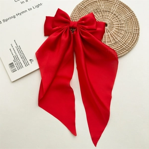 Close-up of large red satin bow hair clip with elegant long ribbons on a white background