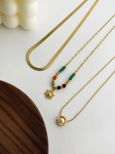 Flat herringbone chain and gold necklaces with sun and pearl charms on white background