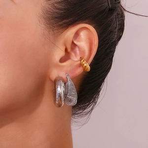 Close-up of a model wearing silver chunky hoop earrings and a gold textured ear cuff