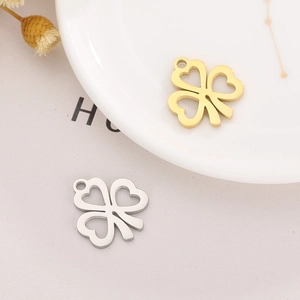 Detail of heart-shaped hollow clover pendants in gold and silver finish on white ceramic