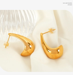 Detailed close-up of 18K gold-plated teardrop earrings on textured white fabric